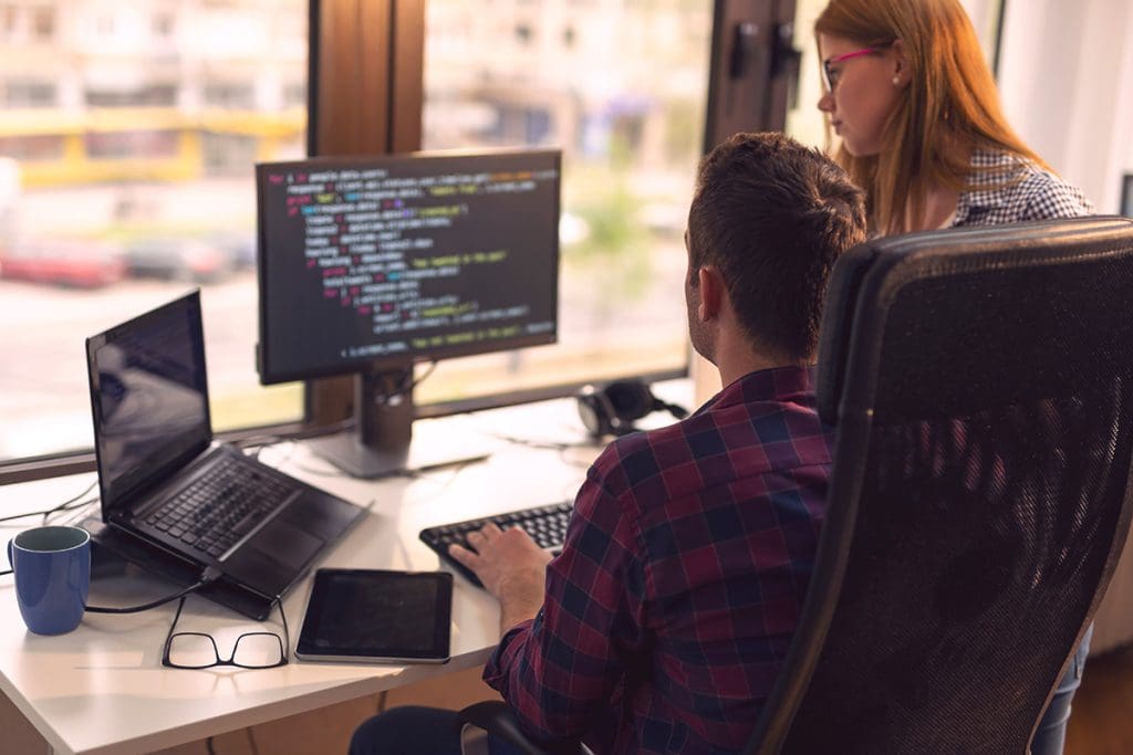 Two people working on code on a computer.